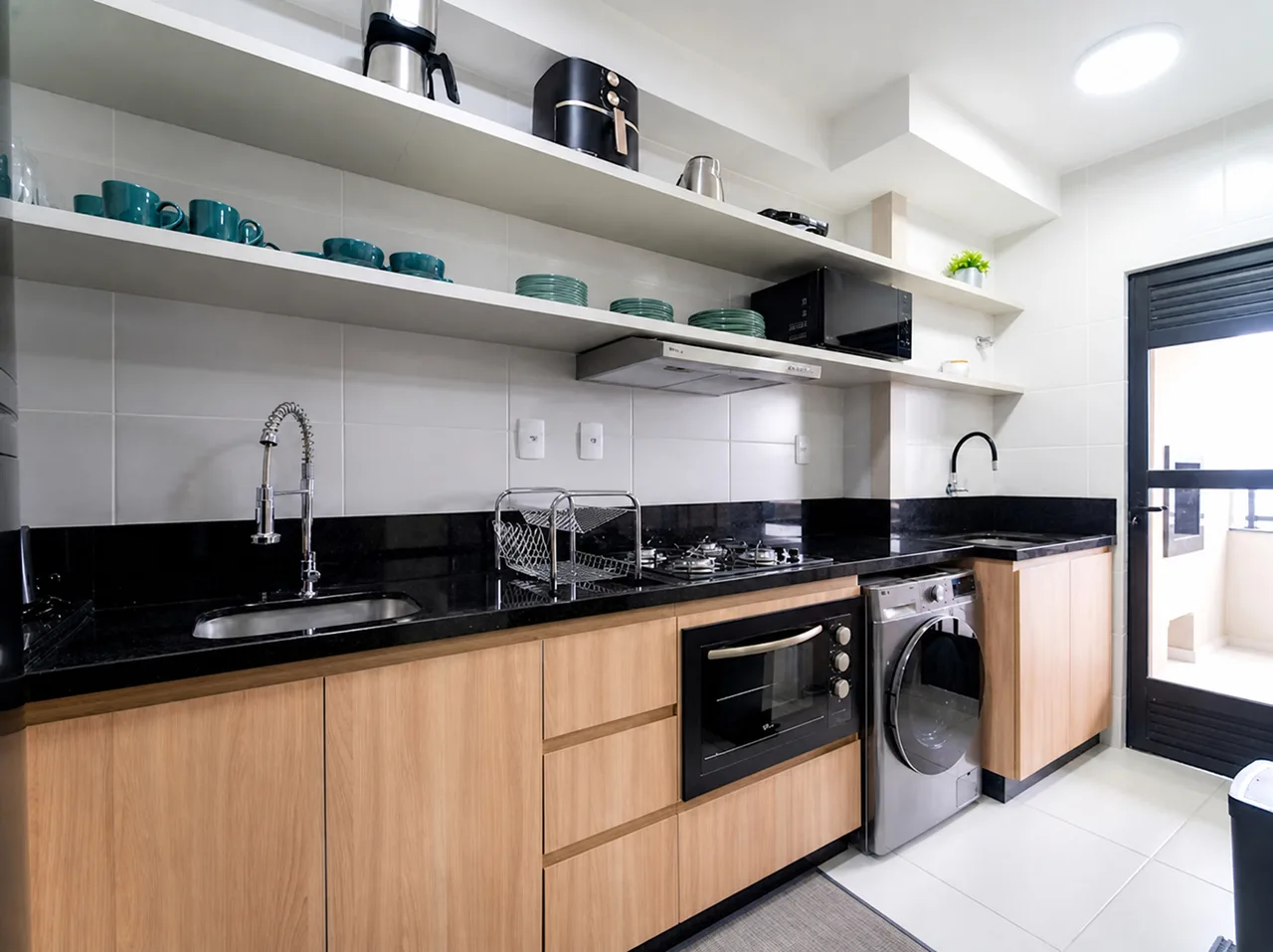 Bancada de granito preto com pia, cooktop e louça nas prateleiras acima