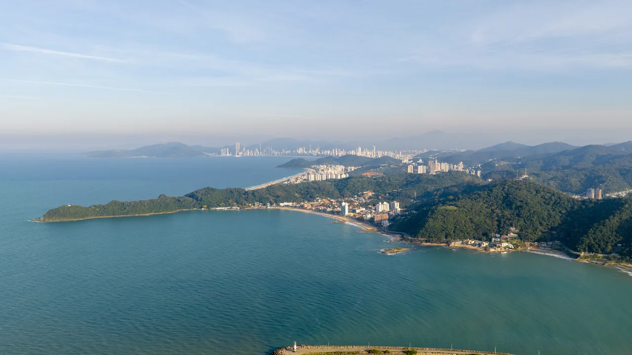 Vista aérea do litoral de Penha, com a ponta do morro, a enseada e Balneário Camboriú ao longe