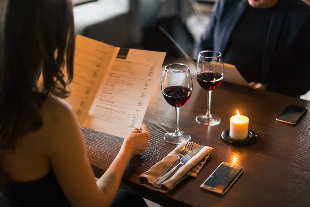 Casal em jantar à luz de velas no restaurante escolhendo o menu com taças de vinho tinto