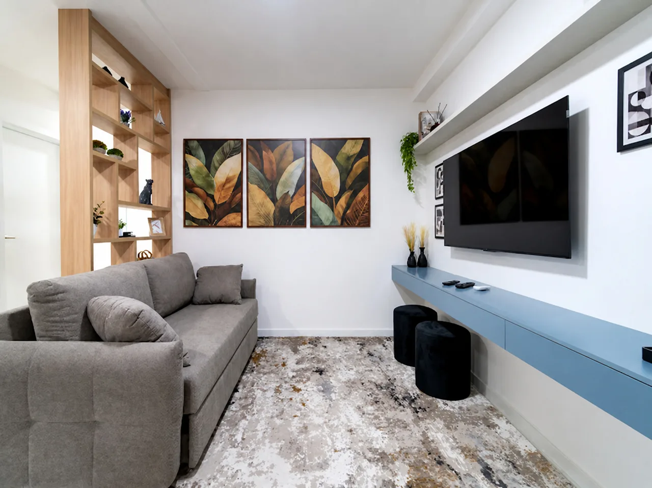 Sala de estar com sofá de canto, tapete claro, Smart TV na parede e estante de madeira