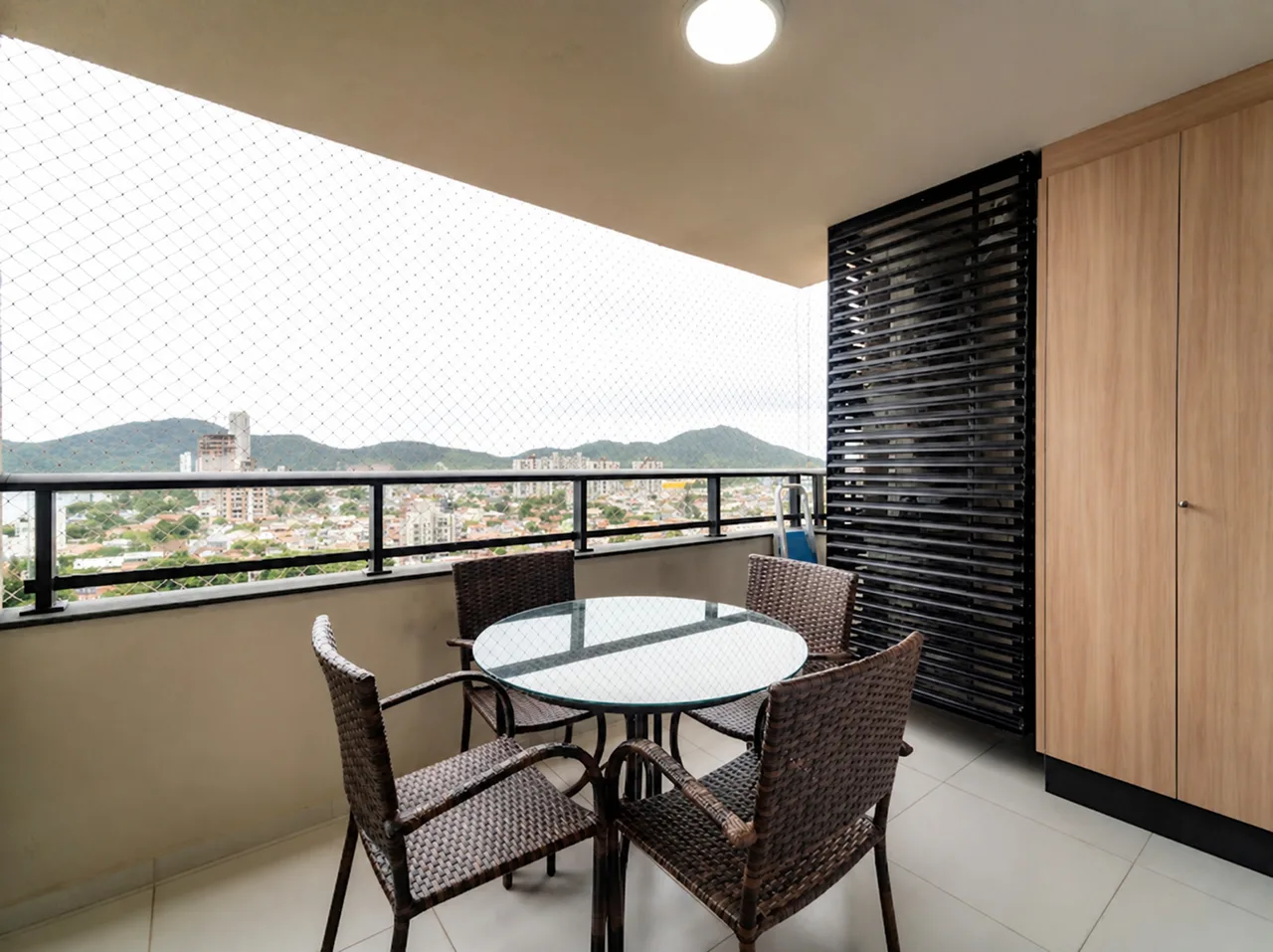 Mesa de vidro com quatro cadeiras de fibra na varanda, de frente para a vista